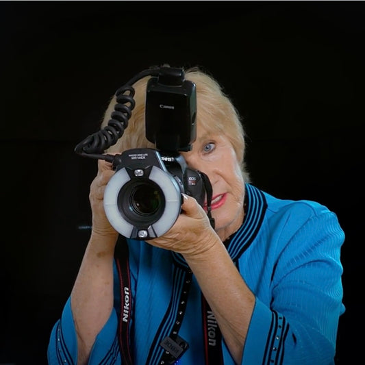 Photo of Rita Bauer holding camera to her eye depicting her teaching dental photography to dental CE students.